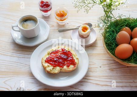 Easter breakfast, bun or sandwich with red cherry jam, boiled egg, coffee and a basket with brown eggs on a wooden table, holiday morning meal, select Stock Photo
