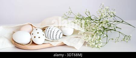 Decorated Easter eggs in a napkin on a wooden tray and some flowers against a light background, panoramic format, holiday banner, soft colors, copy sp Stock Photo
