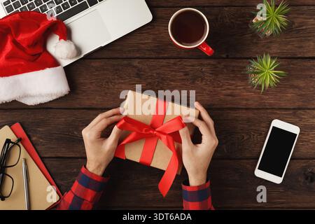 Gift Wrapped With Red Bow on a Wooden Table With Laptop and Coffee Cup During the Holiday Season Stock Photo