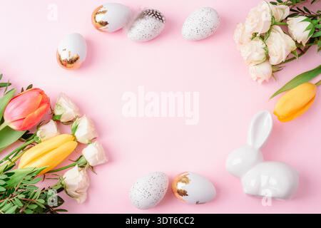Easter background with decorated eggs, ceramic bunny and spring flowers arranged around empty center on pastel pink backdrop. Top view, flat lay, copy Stock Photo