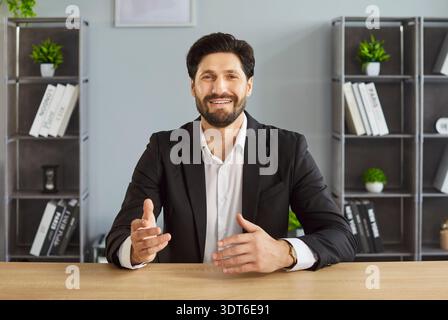Smiling businessman sitting at desk and gesturing while sharing ideas during office meeting. Stock Photo