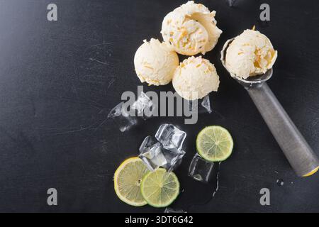 Three Scoops of Lemon Ice Cream on a Black Surface With Ice Cubes and Lime Slices Visible Stock Photo