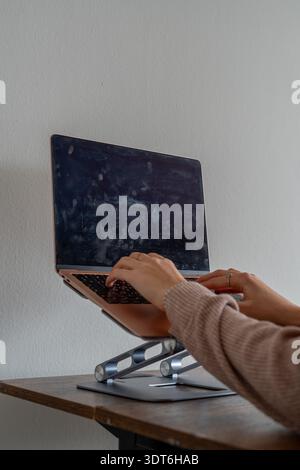 Close-up of female hands typing on a pink laptop placed on an ergonomic stand, with a dirty, smudged screen visible. Realistic workspace scene Stock Photo