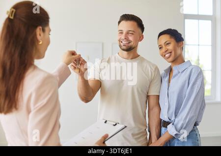 Real estate agent giving keys from new home apartment to happy couple, clients buy or rent property Stock Photo