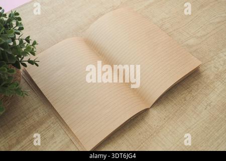 Open notebook placed on wooden table near plant Stock Photo