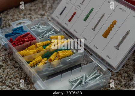 Transparent plastic box filled with metal bolts and plastic wall anchors for mounting into walls. Practical hardware storage scene Stock Photo