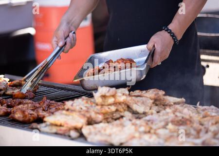 A view of a pit master grilling pieces of chicken. Stock Photo