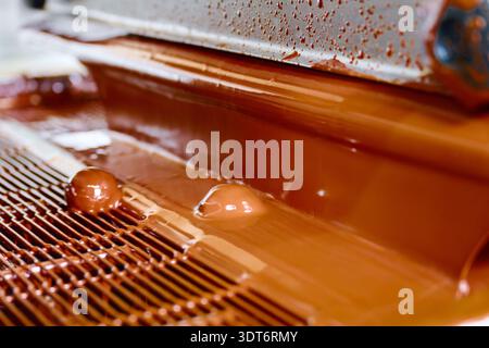 Candy enrobing process showcasing curtain coating technique with chocolate flowing in a manufacturing setting Stock Photo