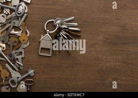 Collection of Various Keys Seen Next to a Keychain With a House Shape on a Wooden Surface Stock Photo