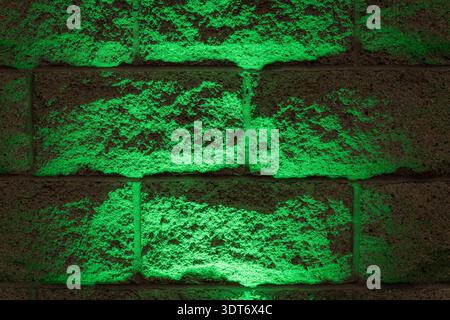Close-up of textured concrete brick wall illuminated by bright green light creating an abstract pattern Stock Photo