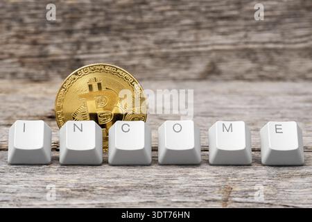 Bitcoin coin and computer keyboard keys arranged to spell INCOME word on the wooden background. Virtual digital currency and financial investment trad Stock Photo