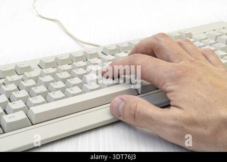 Single hand typing on white keyboard with cable on the white wooden background Stock Photo