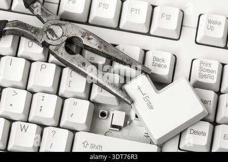 Pliers with ENTER key removed from a keyboard laying on the keyboard. Close up view Stock Photo