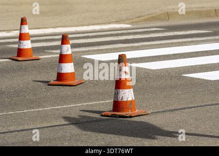 Traffic cones with orange and white stripes standing on street on gray asphalt during road construction works. Just painted white street lines on pede Stock Photo