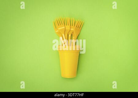 Yellow plastic cup with disposable forks on the green background Stock Photo