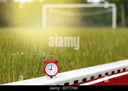 Red alarm clock on the football field with empty gate on background Stock Photo