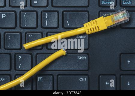 Internet connection disconnected. Computer keyboard with yellow network cable cutted off Stock Photo