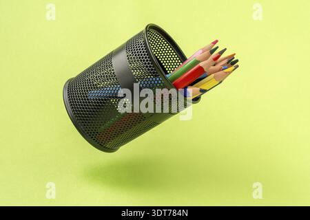 Colored pencils in a black mesh pen pot on a green background Stock Photo