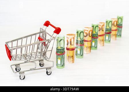 Shopping cart and Euro banknote rolls in one row Stock Photo