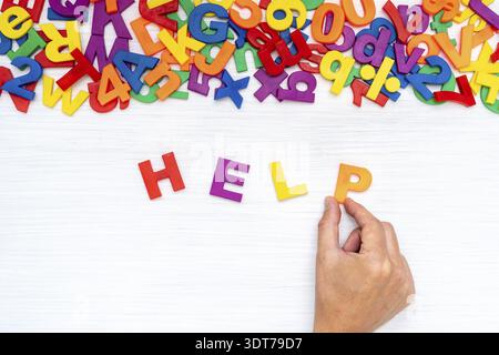 Hand adding letter P to word HELP made of color plastic letters Stock Photo