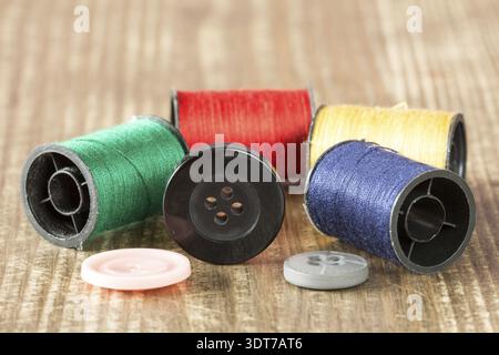 Spools of colored thread and buttons on wooden background Stock Photo