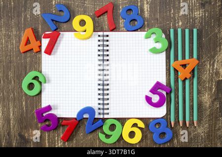 Open notebook with four pencils and colored numbers on the wood background Stock Photo