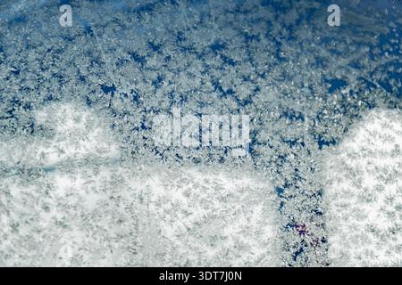 Abstract winter texture of frozen condensation on vehicle glass, intricate ice crystals and snowflake shapes over blurred sky and light reflections Stock Photo