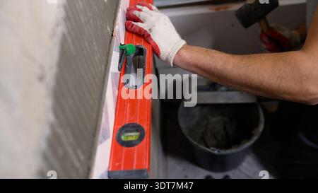 Professional tiler installing new ceramic wall tiles in a bathroom, using a spirit level for perfect alignment Stock Photo