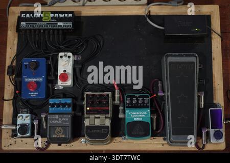 This image showcases a well-organized guitar pedalboard mounted inside a wooden frame. Multiple effects pedals are neatly arranged and interconnected Stock Photo