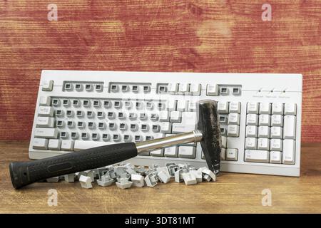Broken computer keyboard and hammer on wooden background. Hammer and computer keyboard with damaged keys Stock Photo