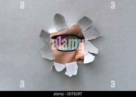 Man in glasses peeping through hole on paper. Male in color glasses looking through hole Stock Photo