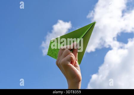 Child hand with green paper plane against blue sky Stock Photo