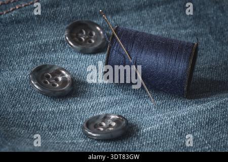 Needle, buttons and spool of thread on jeans fabric Stock Photo
