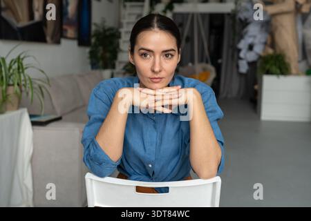 Relaxed thoughtful female artist sits in chair in studio engaged in thinking , art hobby therapy. Stock Photo