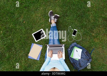 Working on a Laptop While Sitting on Grass With Various Devices and a Backpack Nearby Stock Photo