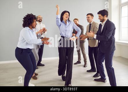 Company employees celebrating success congratulating female colleague indoors. Stock Photo
