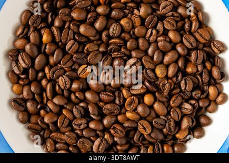 Overhead view of a ceramic bowl filled with premium dark roasted coffee beans isolated on white background for cafe branding and menu. Stock Photo