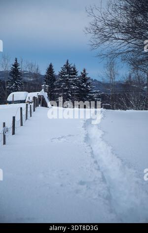 Snow-covered bench on mountain summit above inversion clouds with moon in Norway twilight Stock Photo