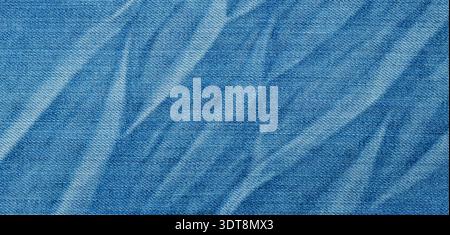 Blue denim fabric showing a textured surface with faded crumpled folds Stock Photo