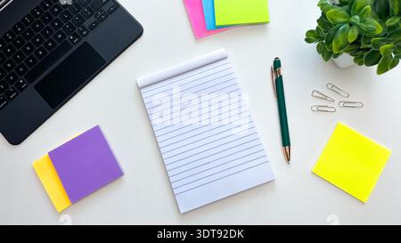 A blank notepad, pen, colored sticky notes, laptop, and paper clips on a white table. Concept for planning, task organization, and productivity. Stock Photo