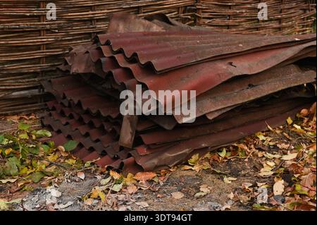 Roofing sheets stacked outdoors in yard, old roofing is out of order, worn out. roofing panels dilapidated with wavy profile lie on ground with fallen Stock Photo