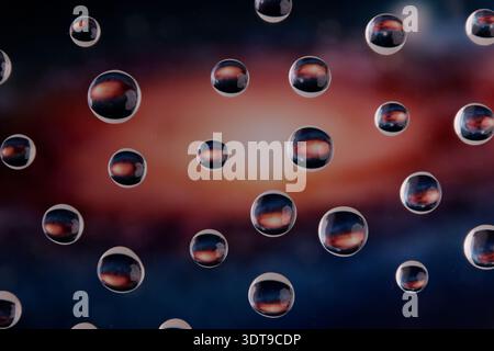 Close-up of transparent water droplets refracting light on glass plate, creating colorful reflections with shallow depth of field and blurred backgrou Stock Photo