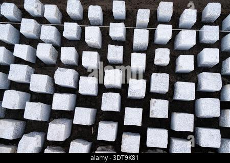 High angle view of granite cobblestones set in sand during street paving work, creating a geometric stone texture background. Stock Photo