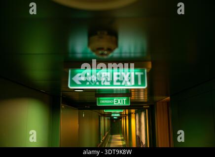 Illuminated Emergency Exit Sign in Dark Corridor Safety Evacuation Direction Concept Stock Photo