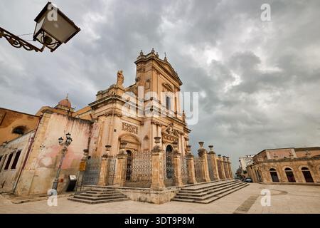 Visitors look at Vincenzo Sinatra's Basilica Santa Maria Maggiore in Ispica, Sicily. The sky is cloudy and the square is quiet. Stock Photo