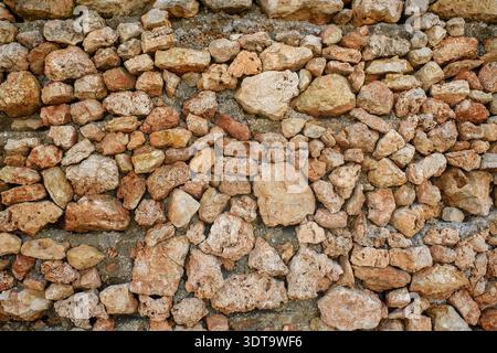 Close-up of an ancient wall made of large natural stones of irregular shape. Detailed texture of stonework in warm earthy tones with a rough surface. Stock Photo