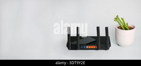 Black wireless router providing network technology for internet connection, placed next to a succulent plant in a minimalist interior. Banner with cop Stock Photo