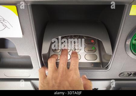 Close-up of a hand entering a PIN code on an ATM keypad for a financial transaction. A person’s hand pressing buttons on a metallic ATM numeric keypad Stock Photo