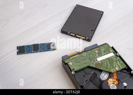 M2 SSD drive placed near SATA SSD and opened hard disk drive on light wooden desk, computer storage components comparison Stock Photo