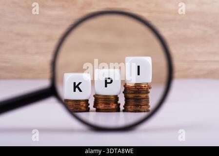 Magnifying glass focus on KPI word on white cube shape on top of gold coins Stock Photo